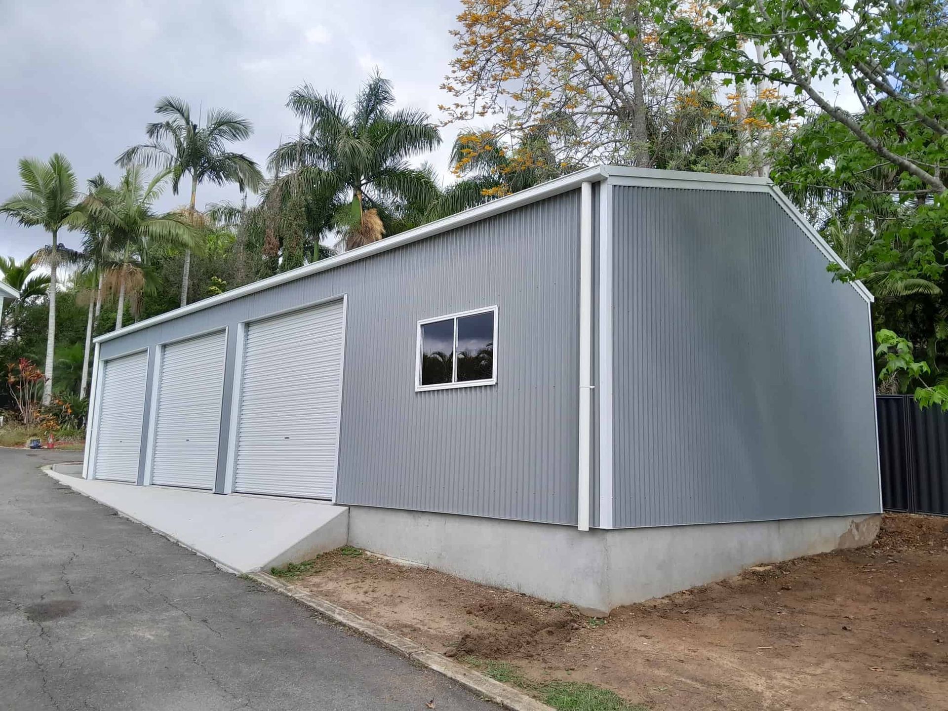 A large gray building with a ramp leading to it is surrounded by trees. — Just Sheds In Kunda Park, QLD