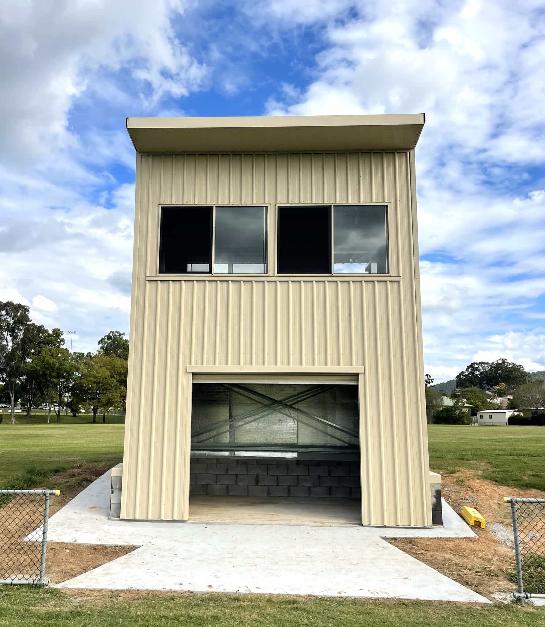 A small building with a garage door is sitting in the middle of a field. — Just Sheds In Kunda Park, QLD