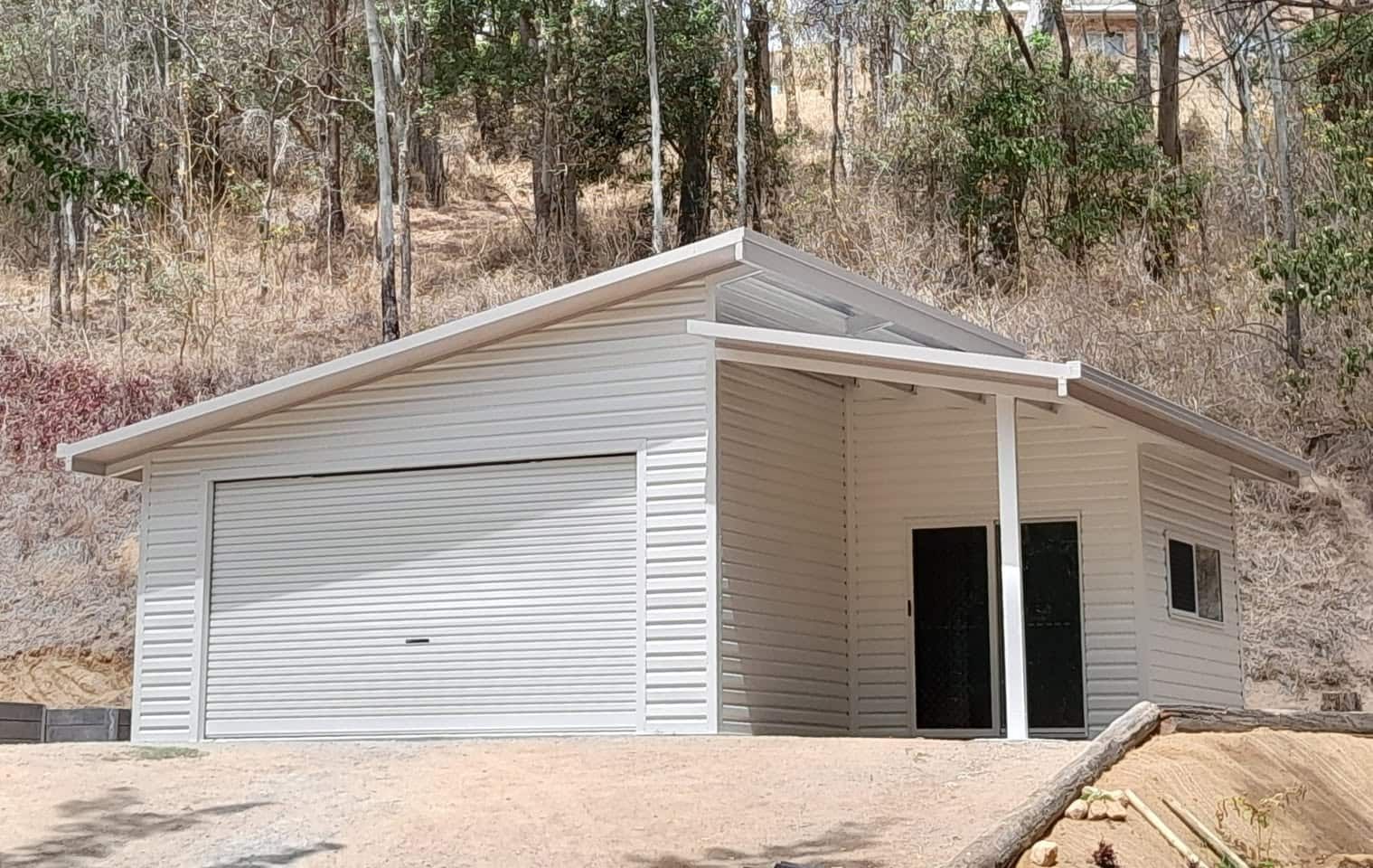 A white garage with a black door is sitting on top of a dirt hill. — Just Sheds In Kunda Park, QLD