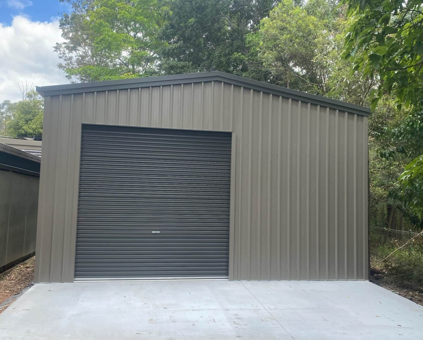 A metal garage with a black garage door and a concrete driveway. — Just Sheds In Kunda Park, QLD