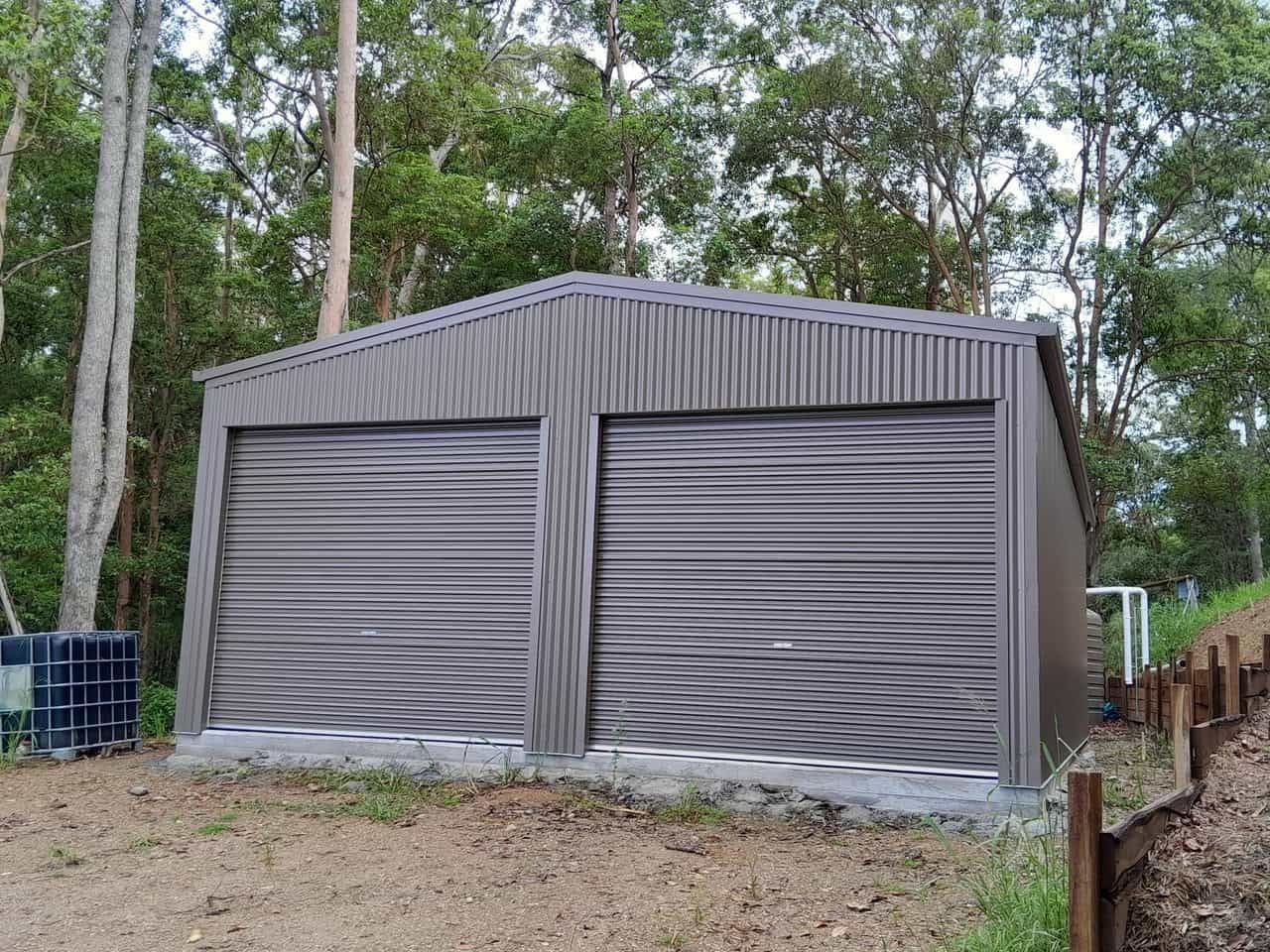 A garage with two garage doors is sitting in the middle of a dirt field. — Just Sheds In Kunda Park, QLD