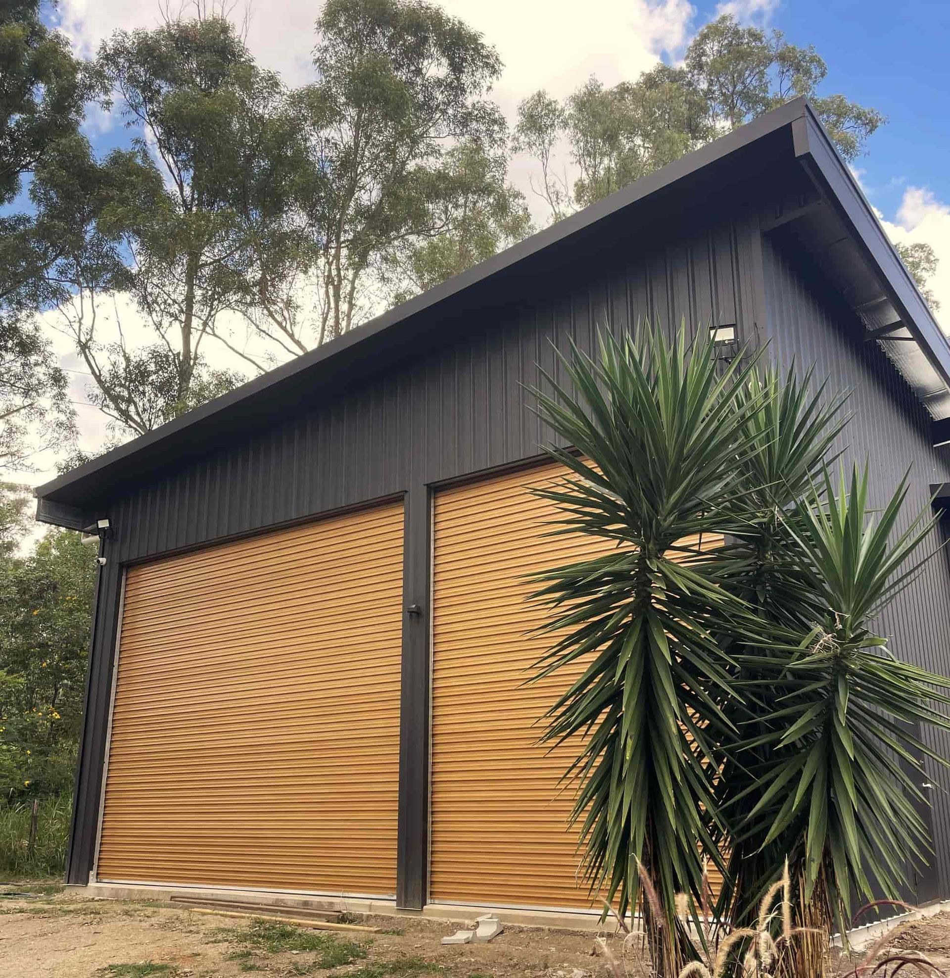 A garage with a wooden door and a palm tree in front of it. — Just Sheds In Kunda Park, QLD