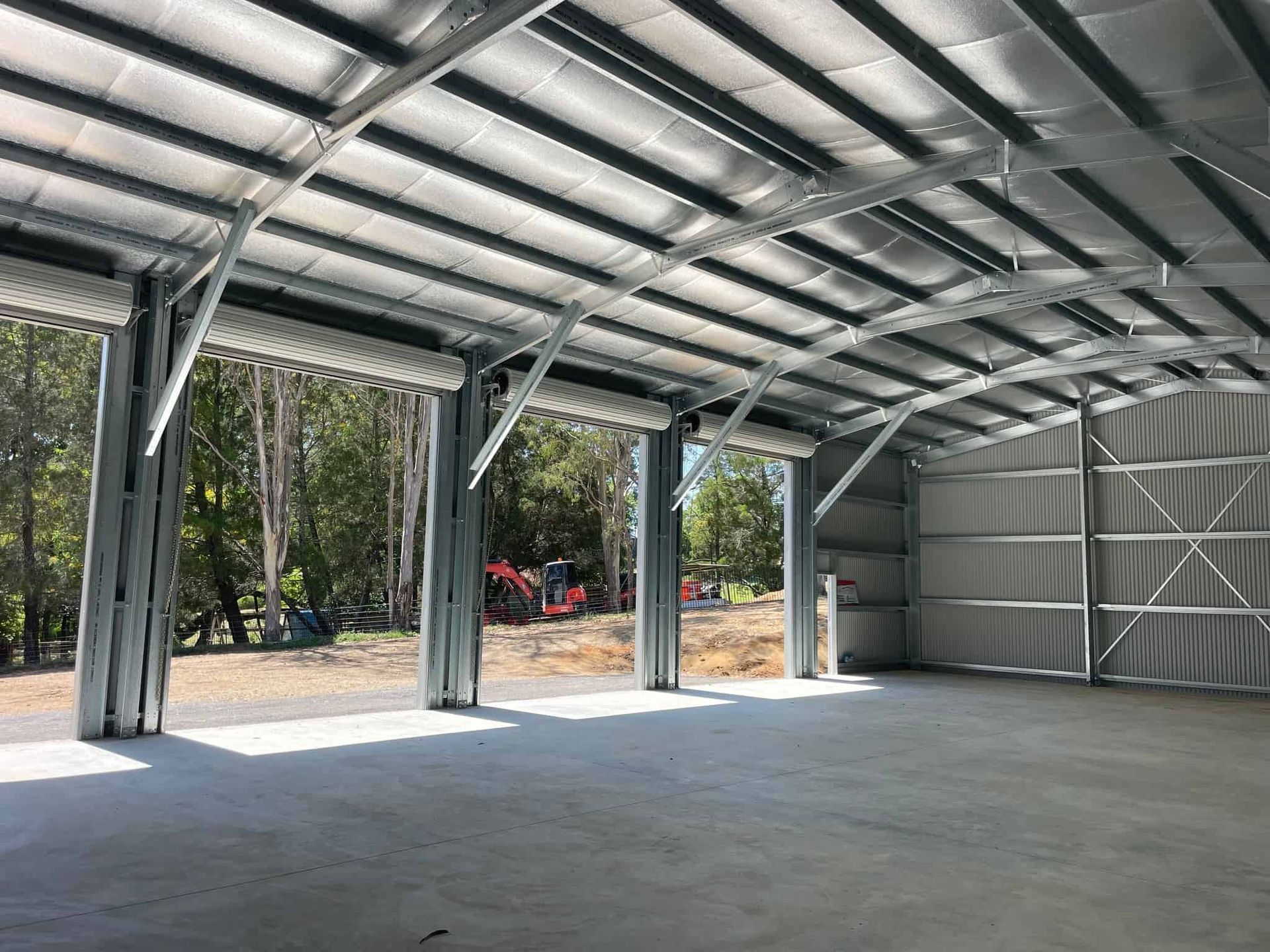 A large warehouse with a lot of doors and a tractor in the background. — Just Sheds In Kunda Park, QLD