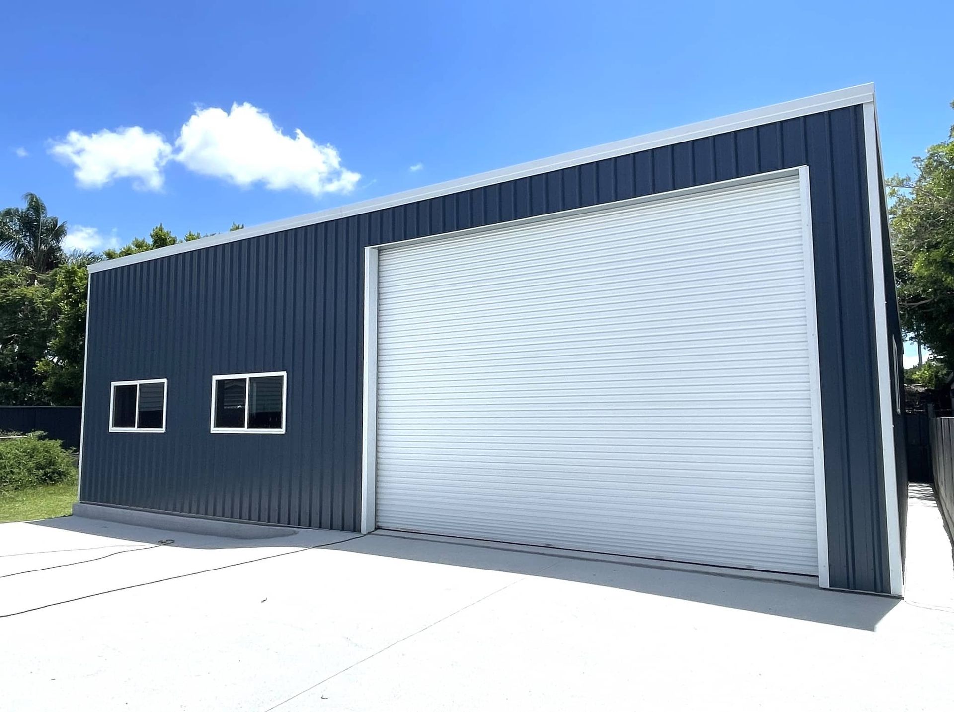 A black building with a white garage door and two windows. — Just Sheds In Kunda Park, QLD