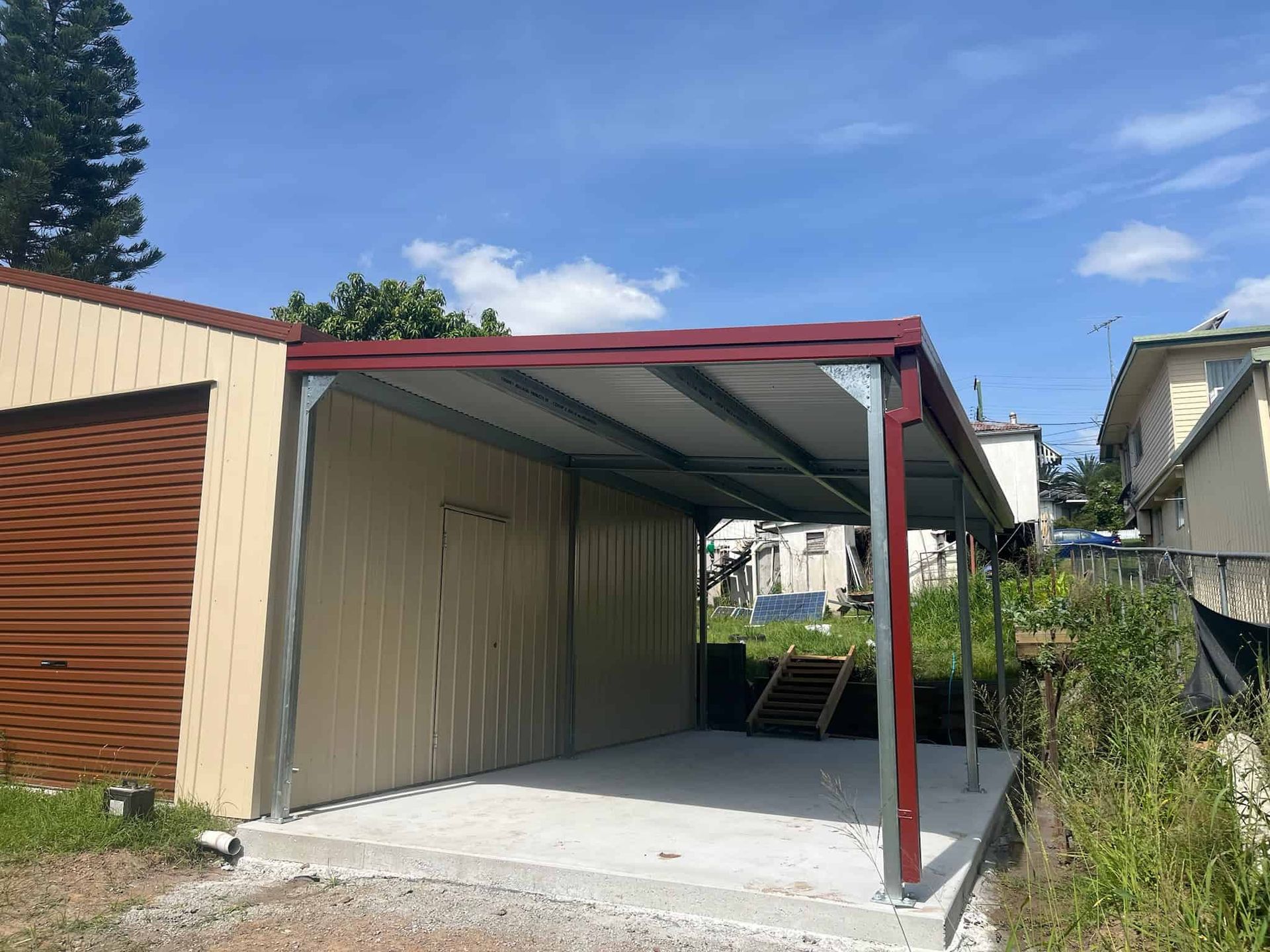 A carport with a red roof is sitting next to a garage. — Just Sheds In Sunshine Coast, QLD