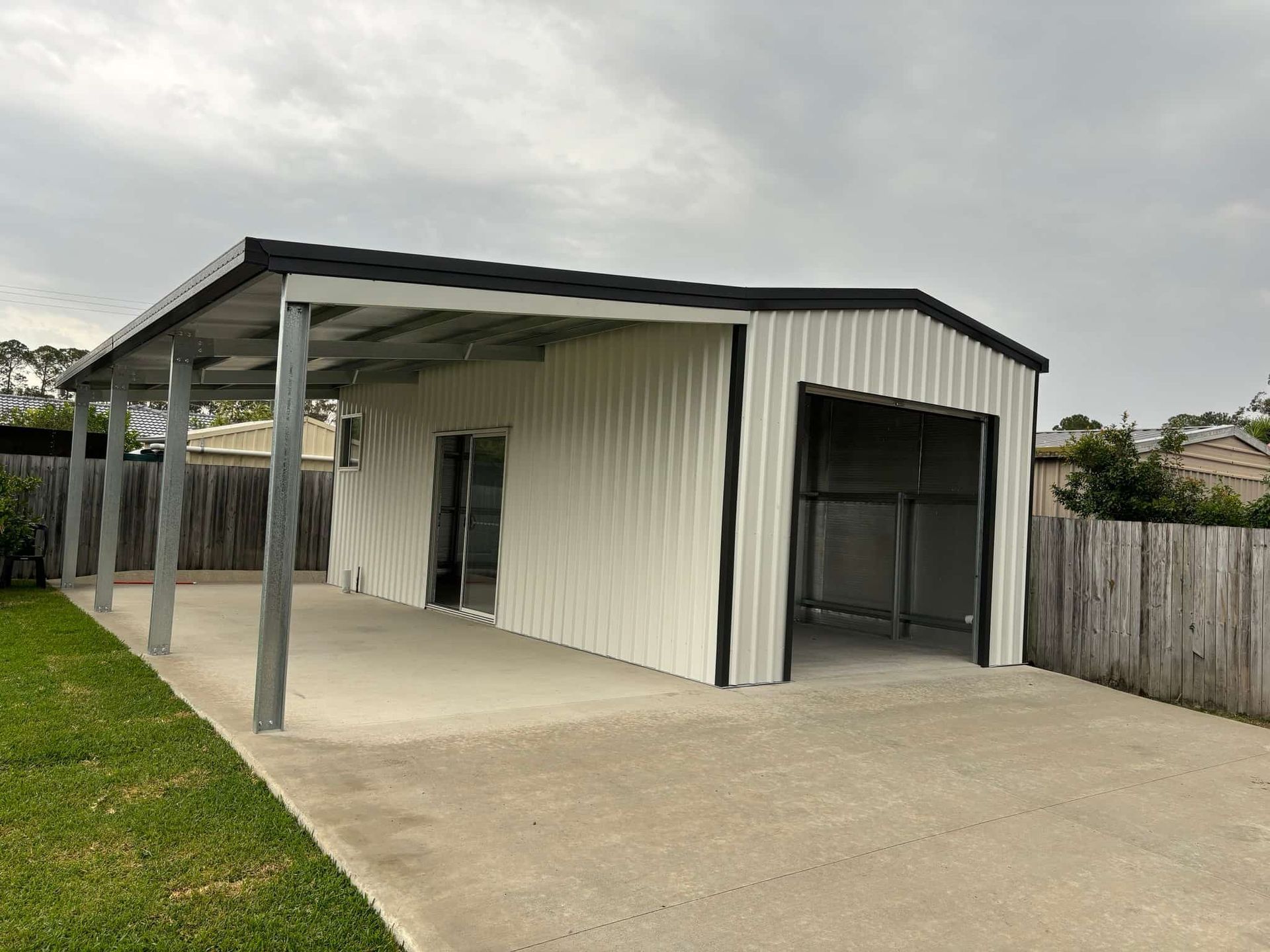 A white garage with a black roof and a covered driveway. — Just Sheds In Kunda Park, QLD