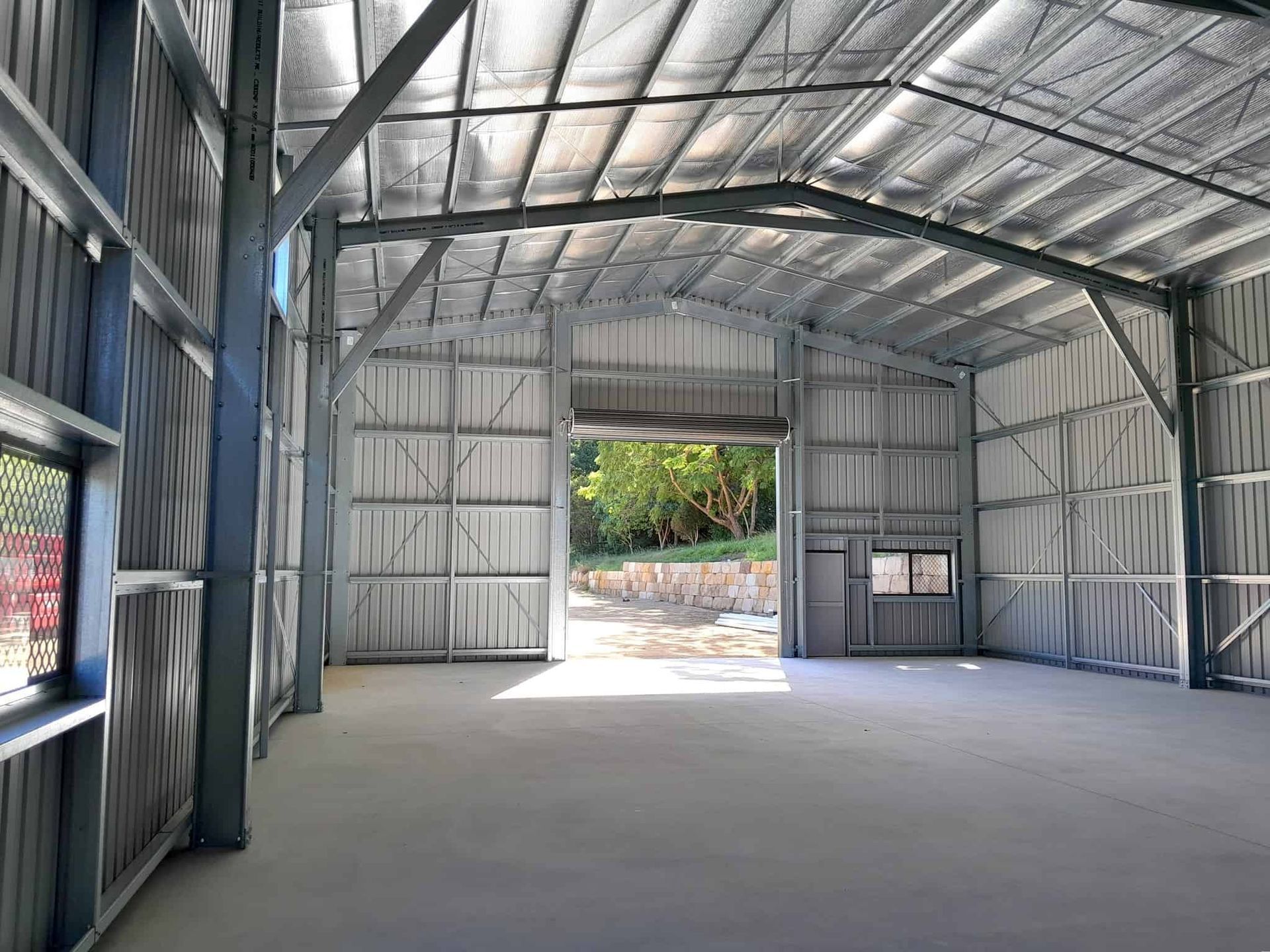A large empty warehouse with a large door open. — Just Sheds In Gympie, QLD