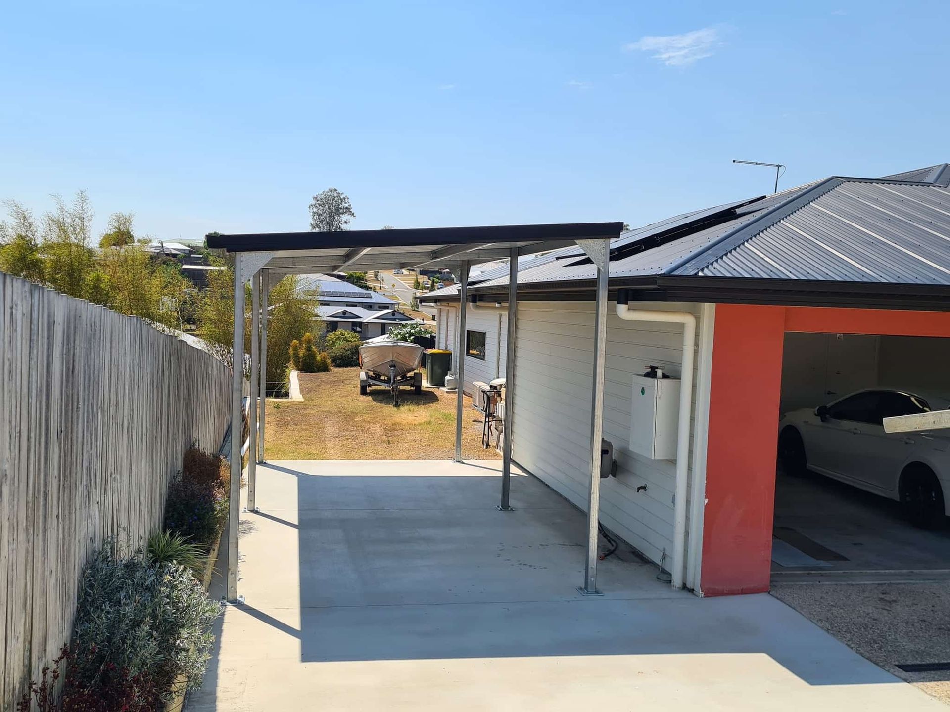 A car is parked in a garage next to a house. — Just Sheds In Brisbane, QLD