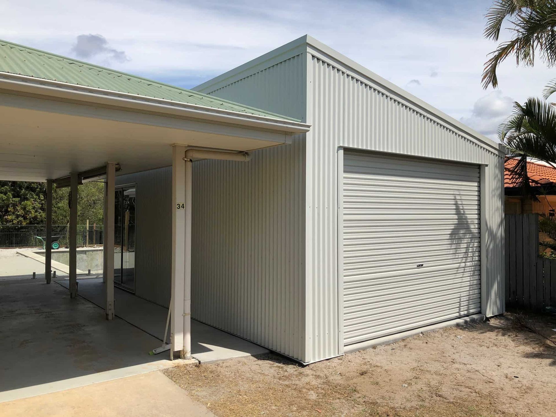 A white garage with a green roof is next to a house. — Just Sheds In Kunda Park, QLD