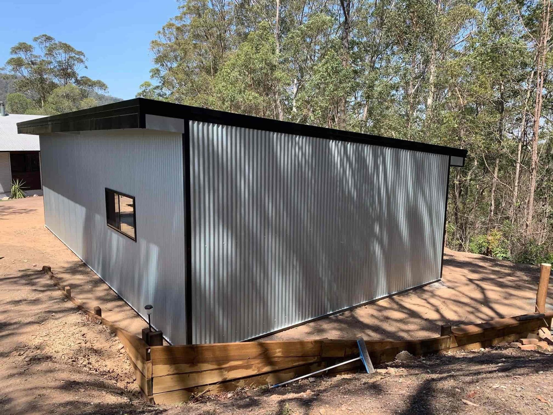 A small metal building with a black roof is sitting on top of a dirt hill. — Just Sheds In Kunda Park, QLD