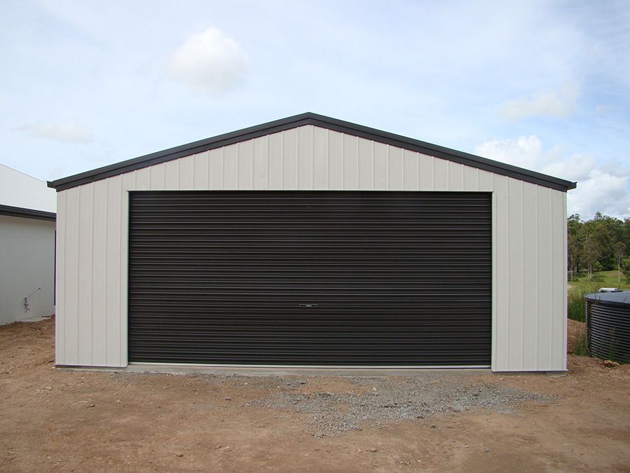 A White Garage With a Black Door is Sitting on Top of a Dirt Field — Just Sheds In Kunda Park, QLD
