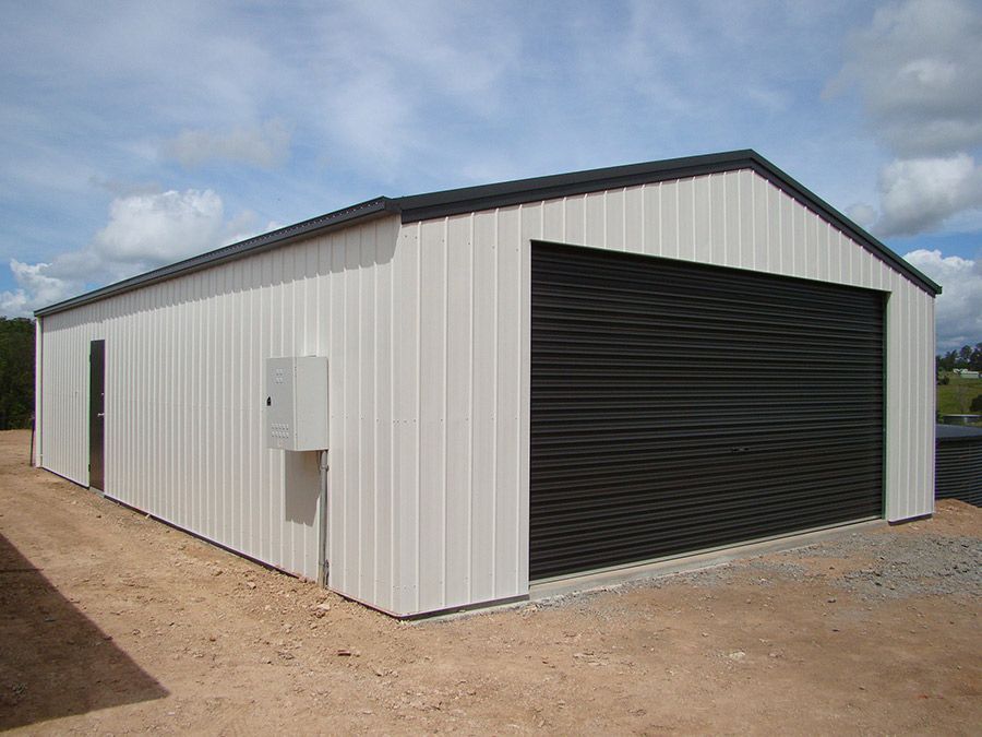 A White Garage With a Black Door is Sitting on Top of a Dirt Field — Just Sheds In Kunda Park, QLD