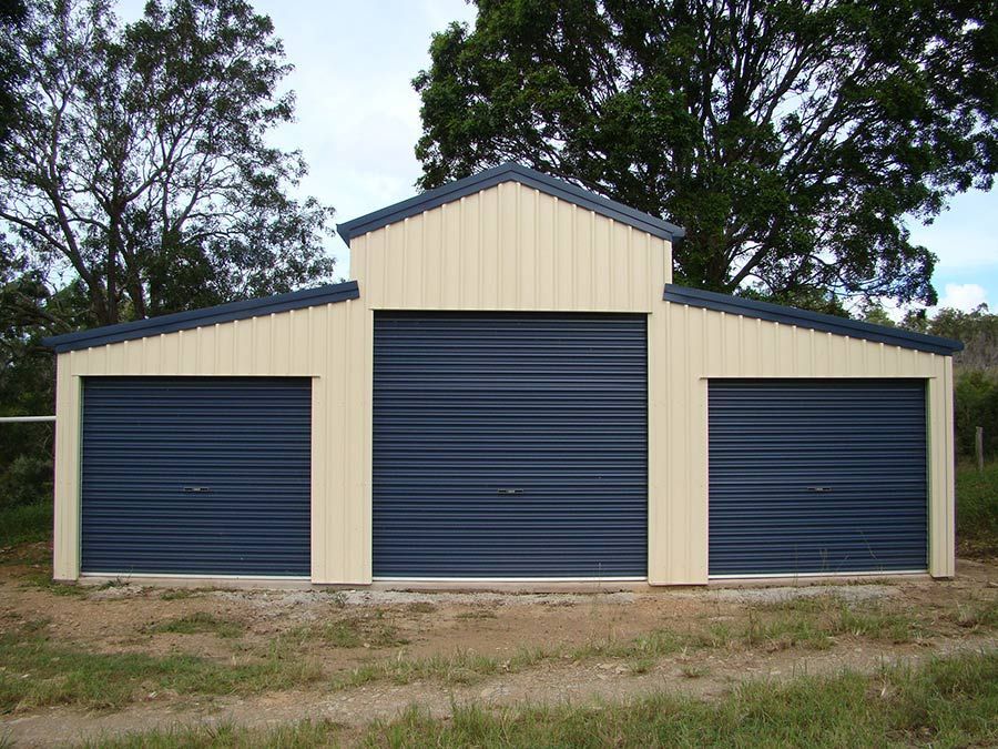 A Garage With Three Blue Doors and Trees in the Background — Just Sheds In Kunda Park, QLD