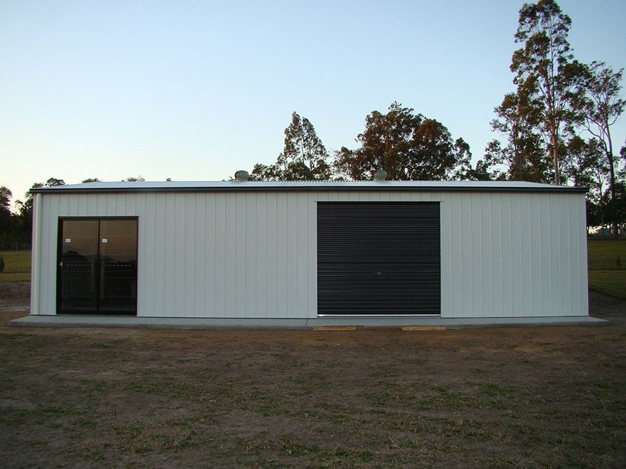 A Large White Building With a Black Garage Door — Just Sheds In Kunda Park, QLD