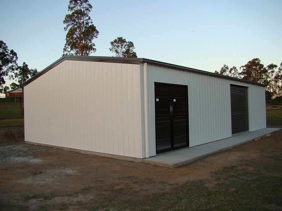 A White Building With Black Doors is Sitting in the Middle of a Field — Just Sheds In Kunda Park, QLD