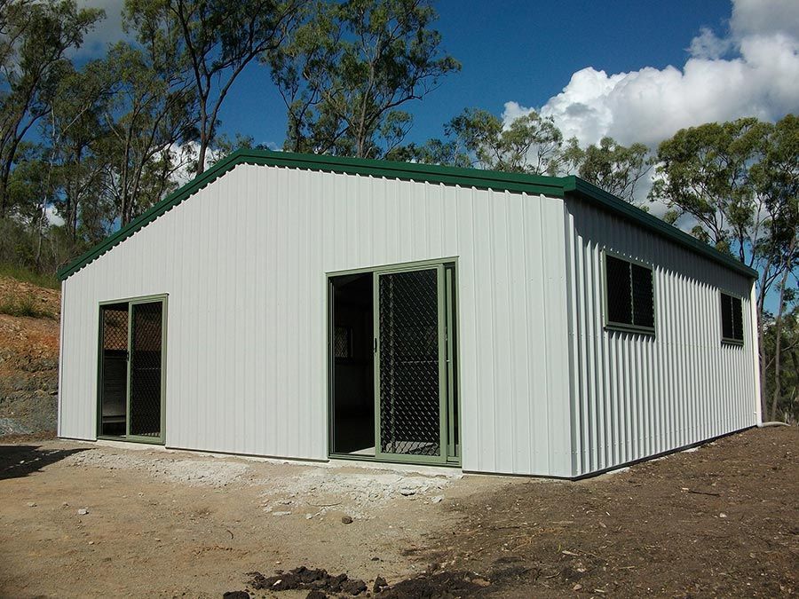 A White Building With a Green Roof is Surrounded by Trees — Just Sheds In Kunda Park, QLD