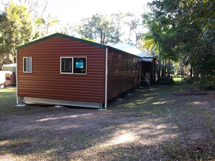 A Brown House With a Green Roof is Sitting in the Middle of a Dirt Field — Just Sheds In Kunda Park, QLD