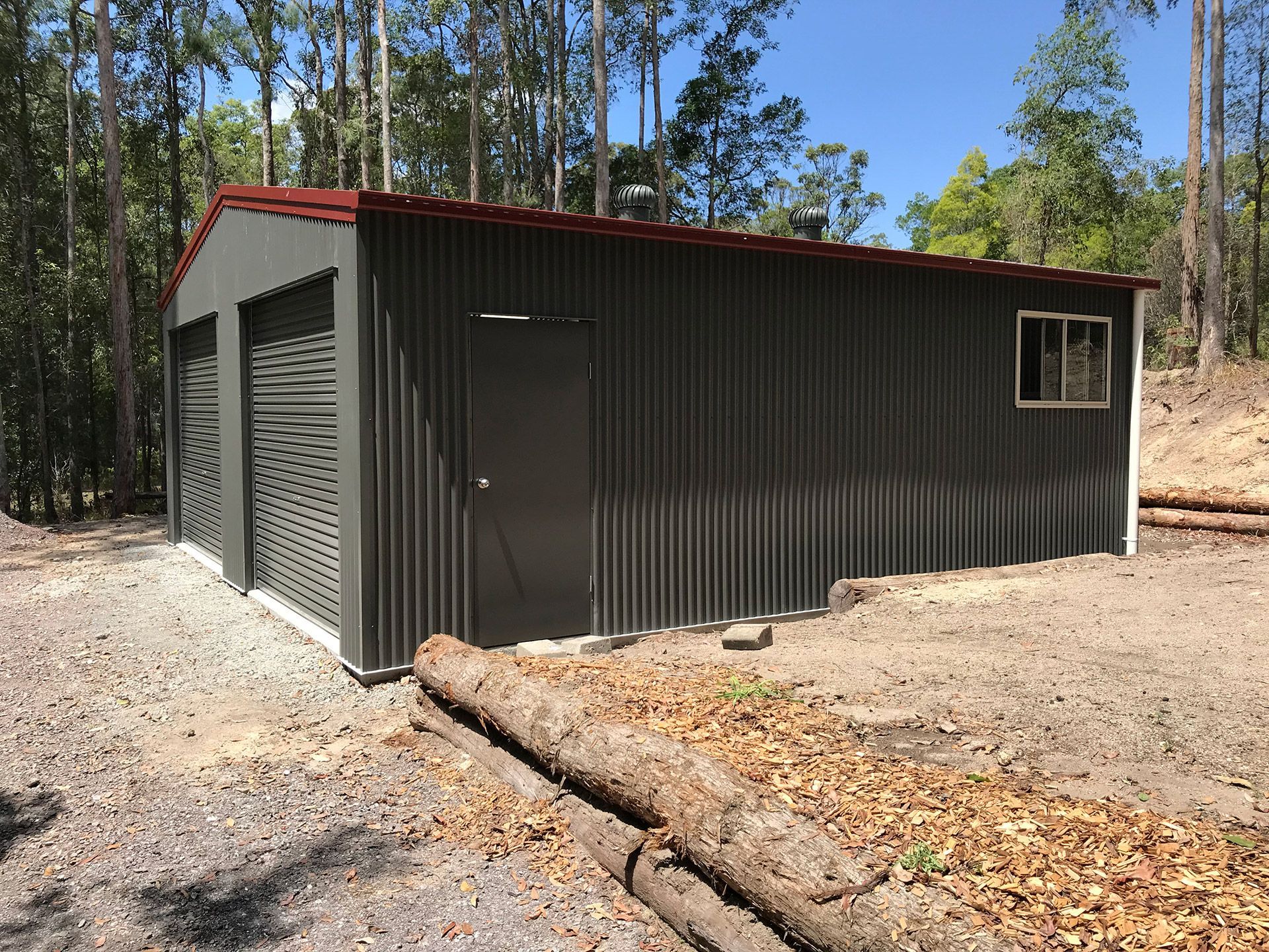 A Large Metal Building With a Red Roof is Sitting in the Middle of a Dirt Field — Just Sheds In Brisbane, QLD