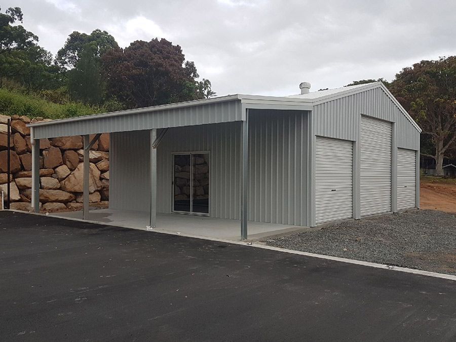 A Large Metal Building With a Porch and Garage Doors  — Just Sheds In Kunda Park, QLD