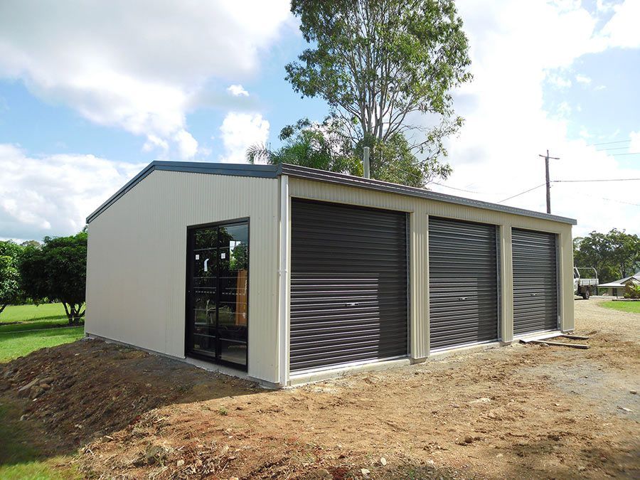 A White Garage With Three Black Garage Doors is Sitting in the Middle of a Dirt Field — Just Sheds In Kunda Park, QLD