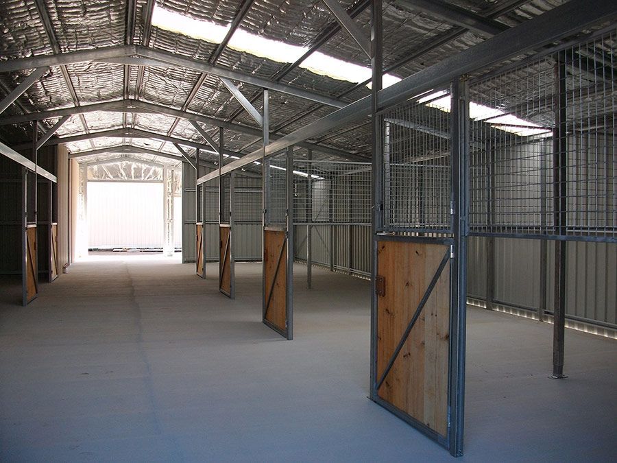 A Large Empty Barn With Wooden Stalls and a Metal Roof — Just Sheds In Kunda Park, QLD