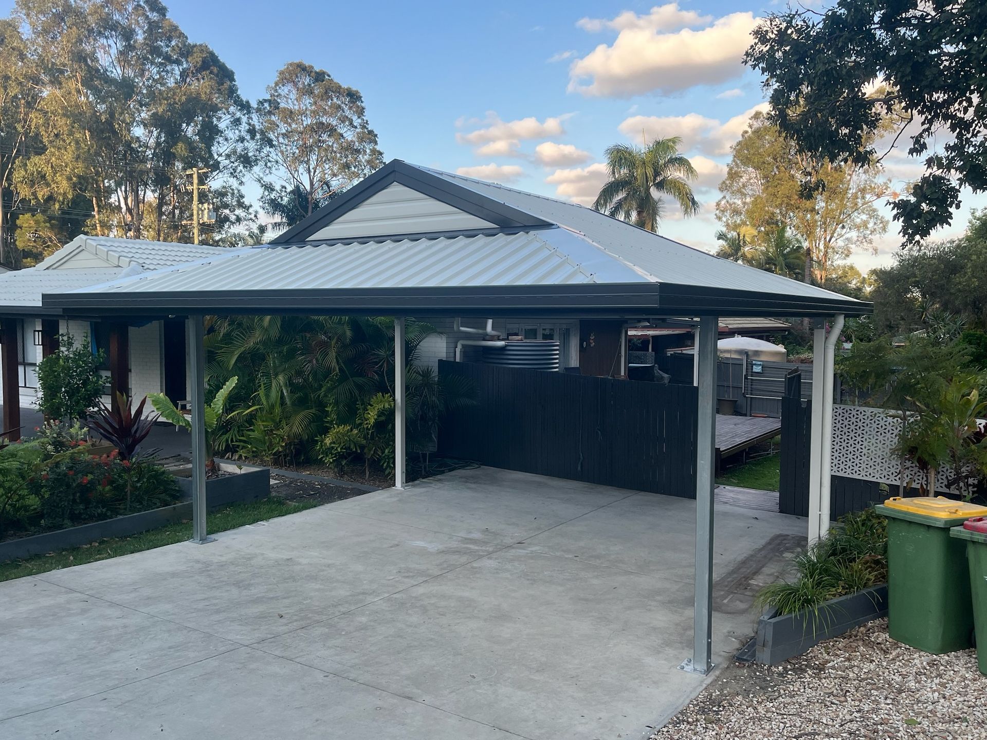 A Concrete Driveway With a Carport, Gray Roof, and a Dark Fence