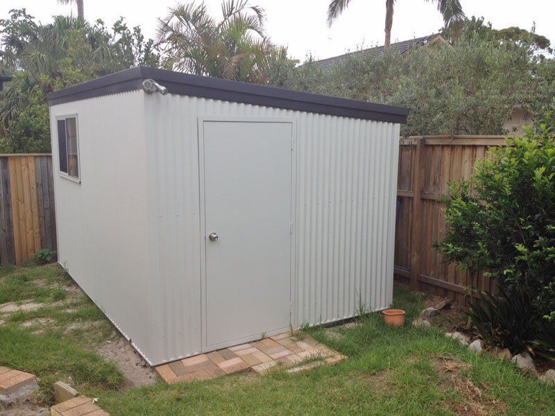 A White Shed With a Black Roof is in a Backyard Next to a Wooden Fence — Just Sheds In Kunda Park, QLD