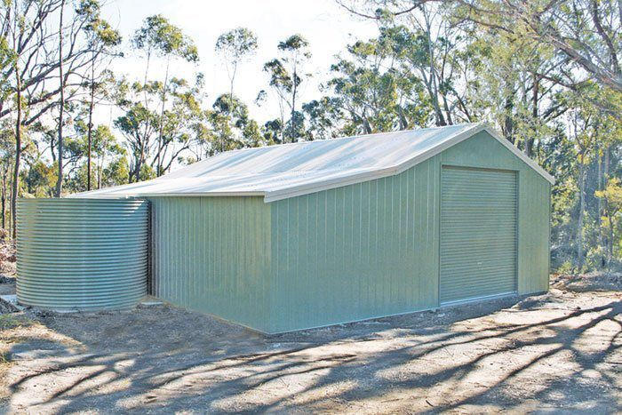 A Green Metal Garage With a White Roof is Sitting in the Middle of a Forest — Just Sheds In Kunda Park, QLD