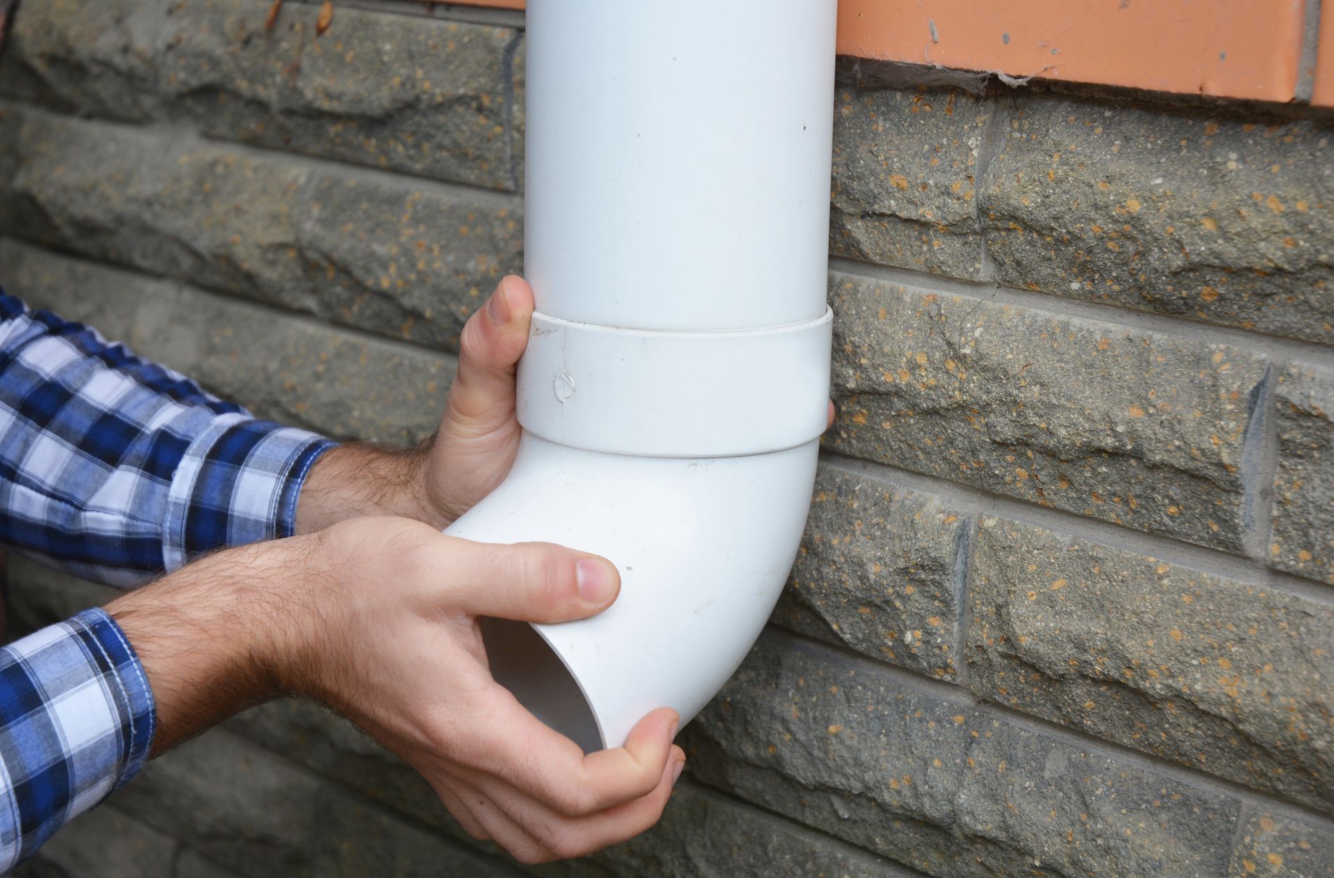 Close-up of a gutter contractor’s hands as he installs a PVC rain gutter drain pipe.