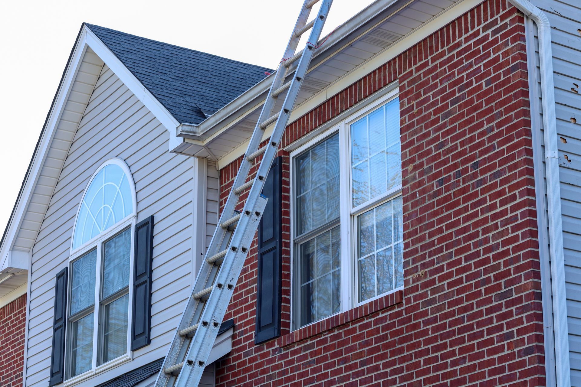 Ladder set against house exterior for gutter replacement near brick and siding walls. Ladder set against house exterior for gutter replacement near brick and siding walls.