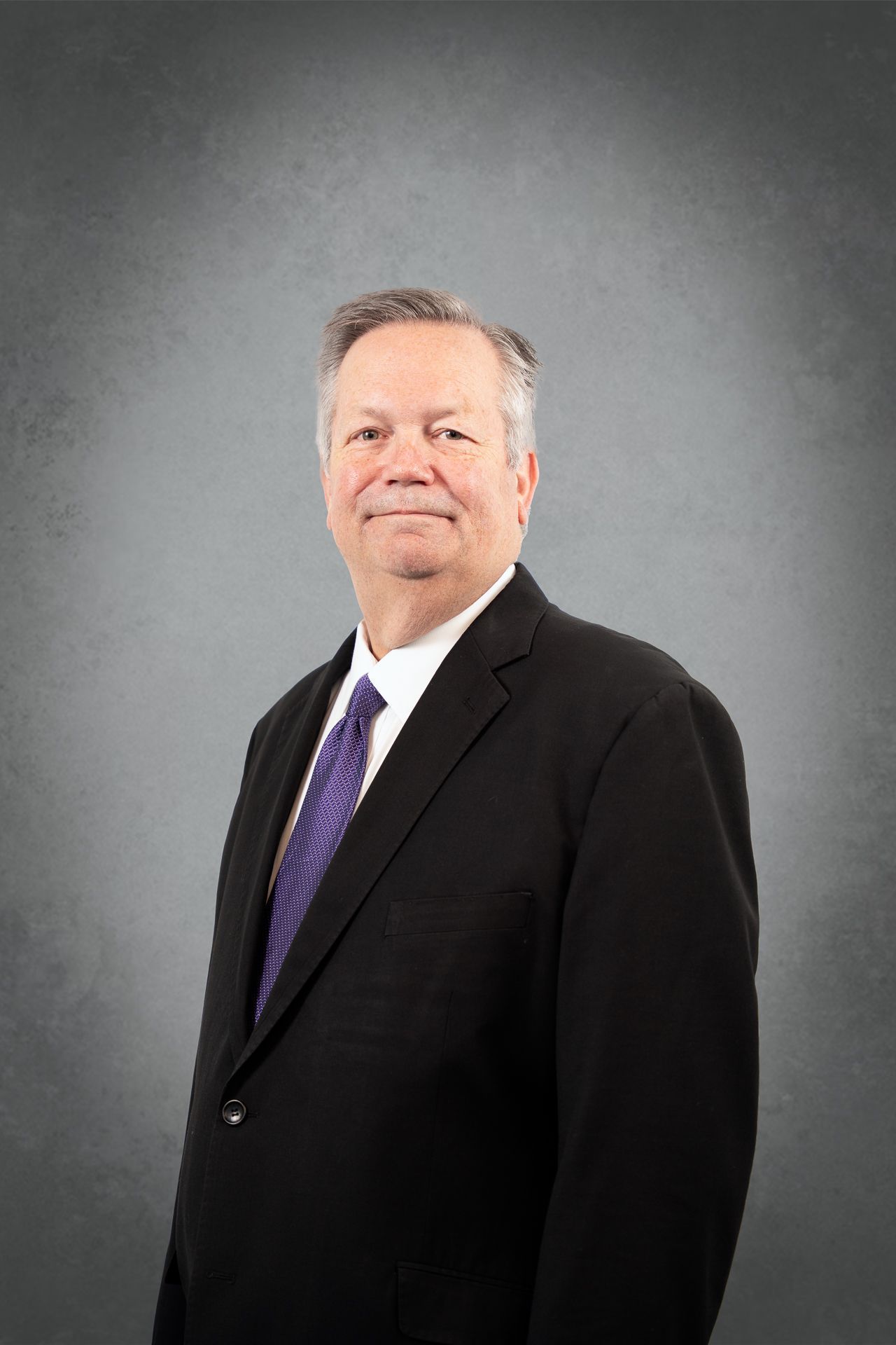 A man in a suit and tie is standing in front of a gray background.