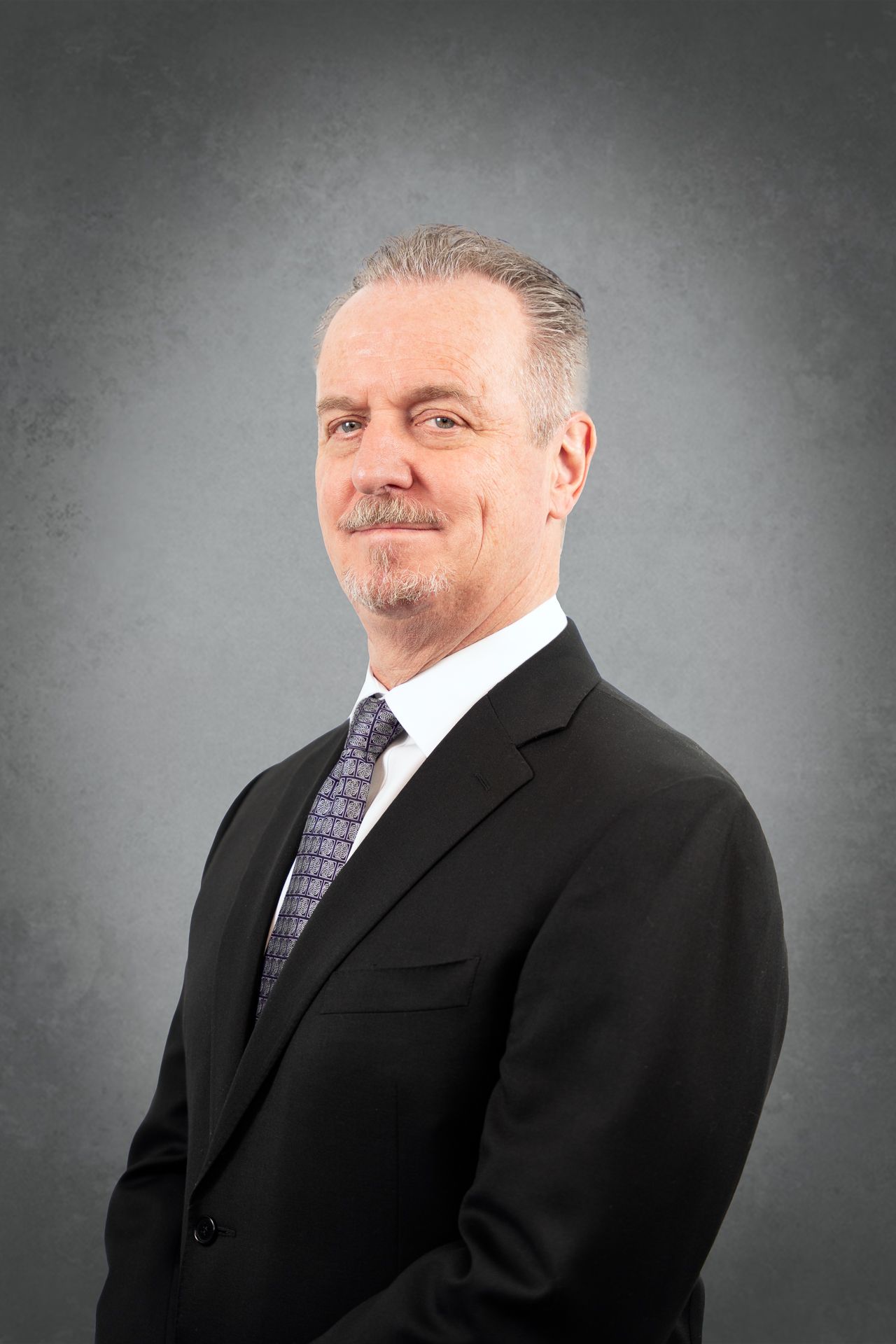 A man in a suit and tie is standing in front of a gray background.