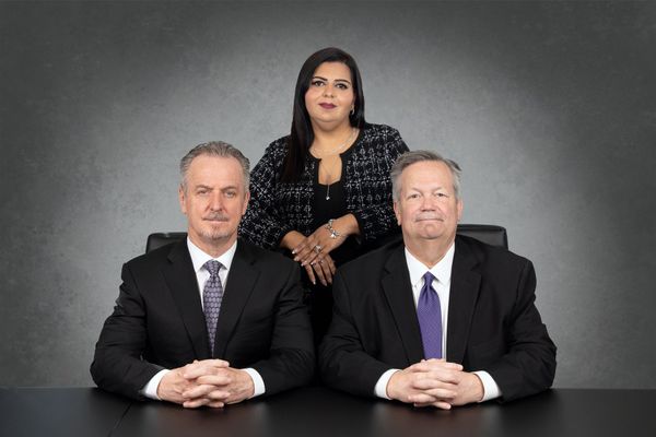 Three business people are sitting at a table with their hands folded.