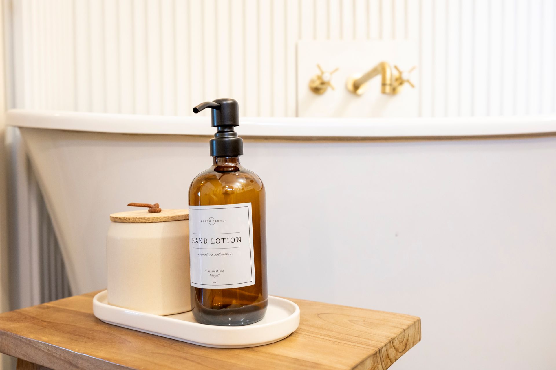 A bottle of soap is sitting on a wooden tray in a bathroom next to a bathtub.