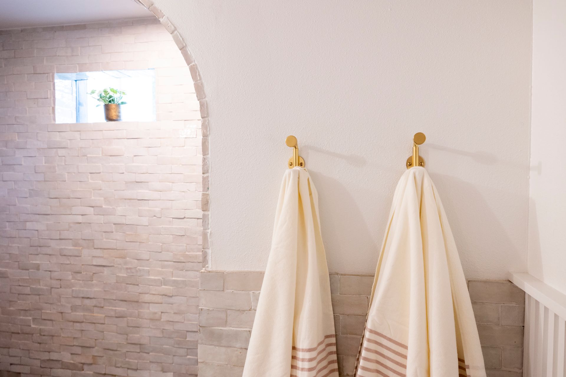 Two towels are hanging on hooks in a bathroom.
