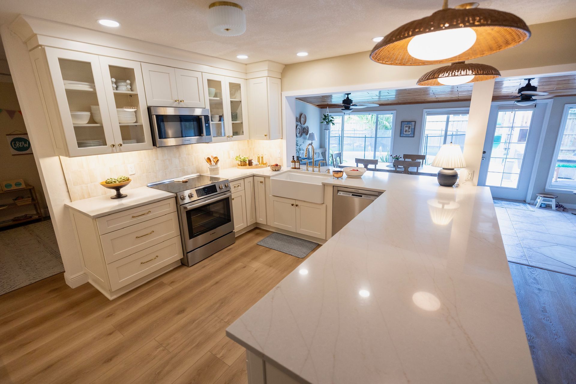 Modern kitchen with white cabinets, stainless steel appliances, quartz island, and light wood flooring.