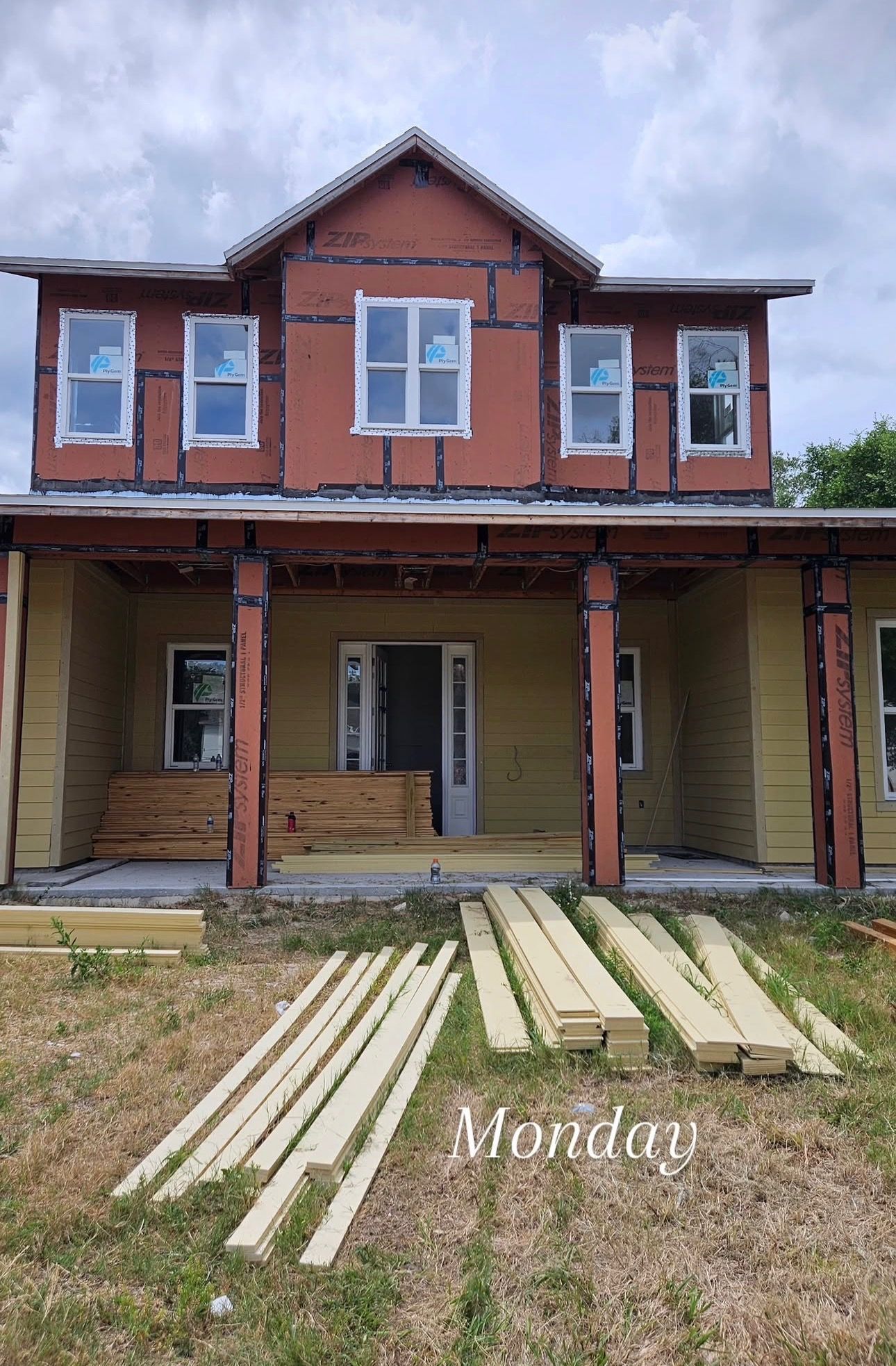 Front view of unfinished two-story red brick house with porch columns and lumber laid in the yard.