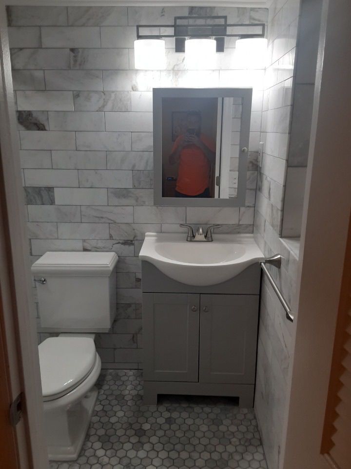 Small white tiled bathroom with toilet, sink, mirror cabinet, and hexagon tile floor.