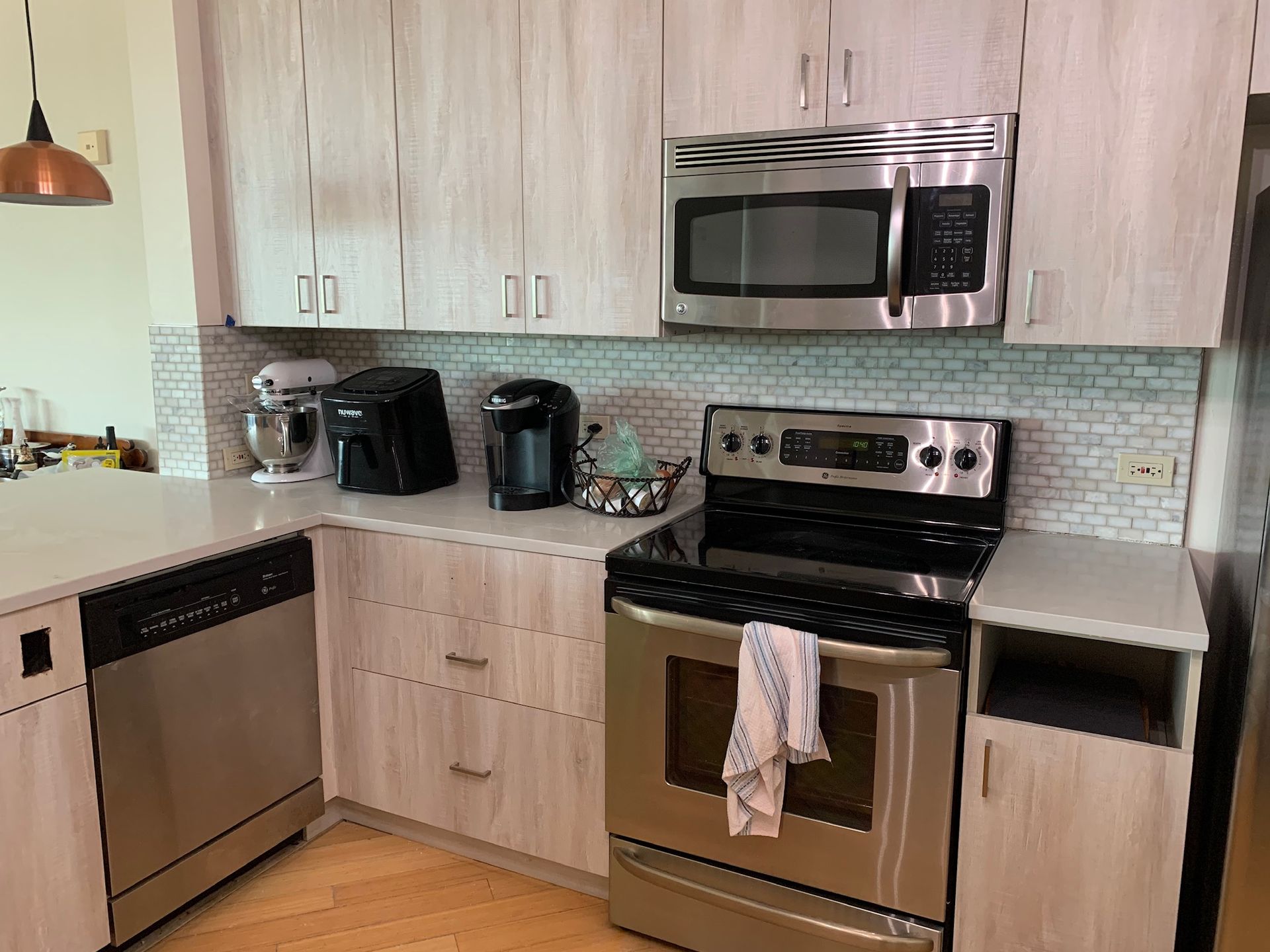 Modern kitchen with stainless steel appliances, light wood cabinets, and a black stove with a towel hanging on it