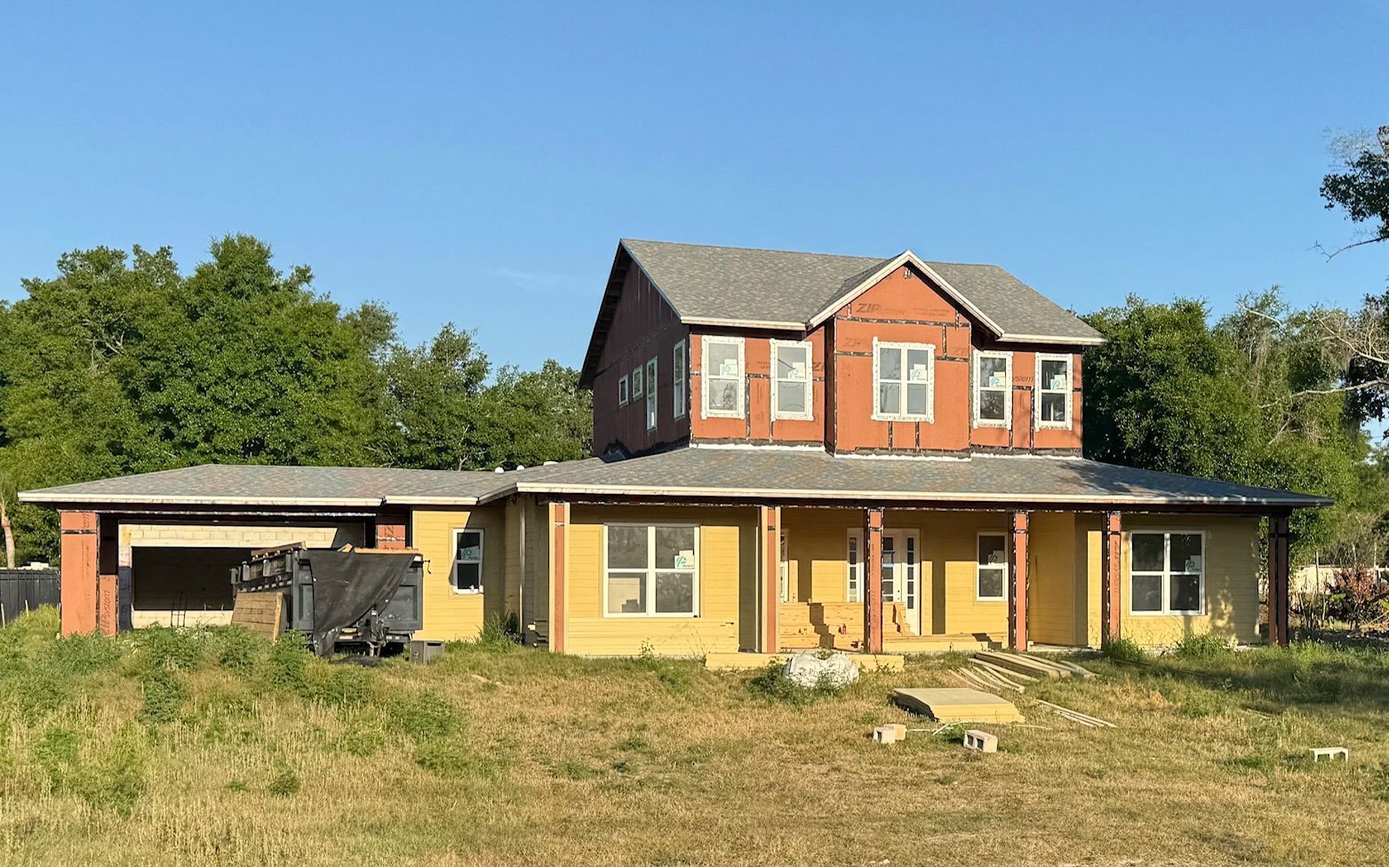 Yellow farmhouse with a red upstairs and a front porch in a grassy field under a blue sky