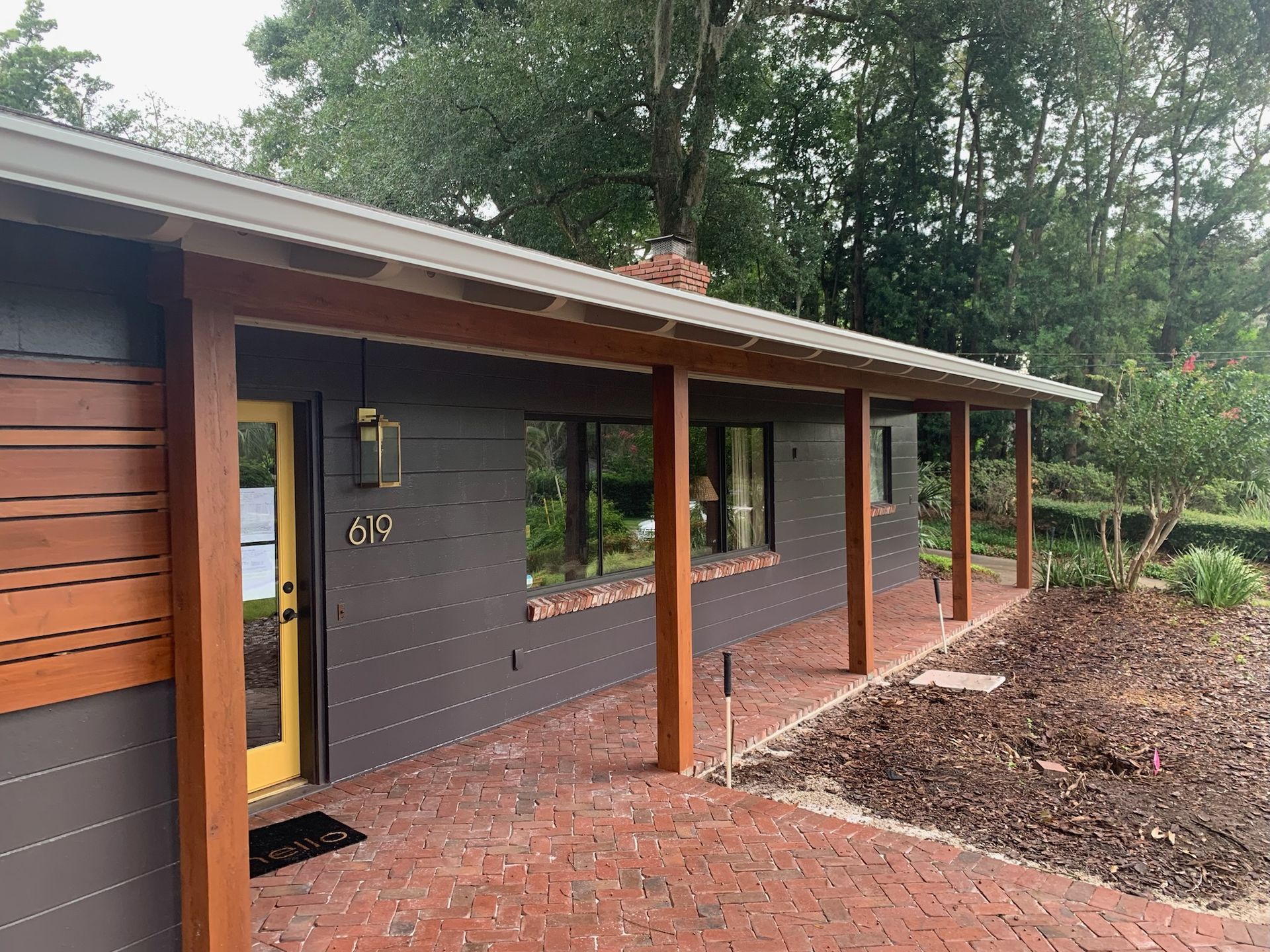 Modern design-build home exterior: Gray siding, wood accents, yellow door, brick path