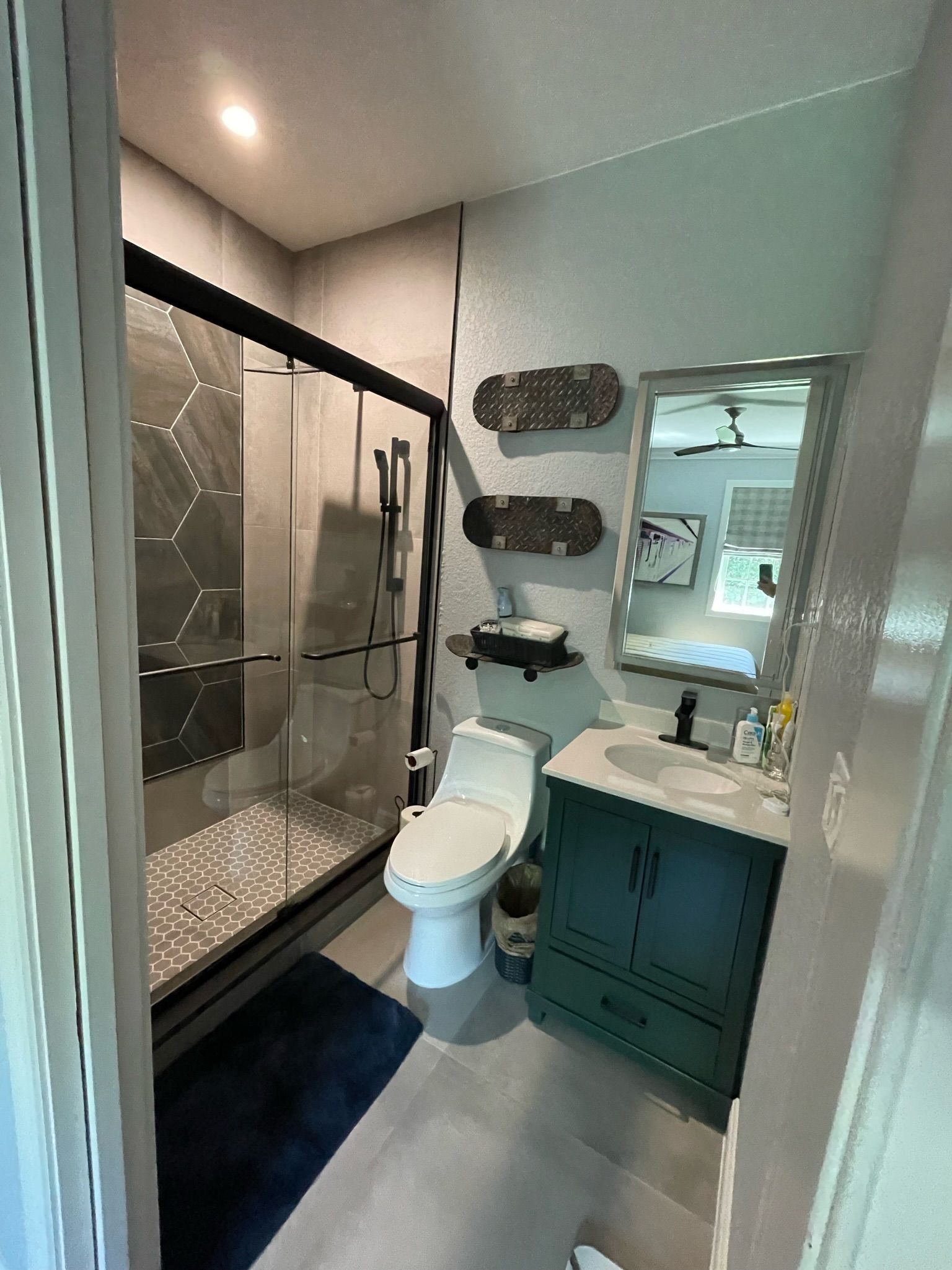 Narrow bathroom with glass shower, toilet, teal vanity, and wall mirror.