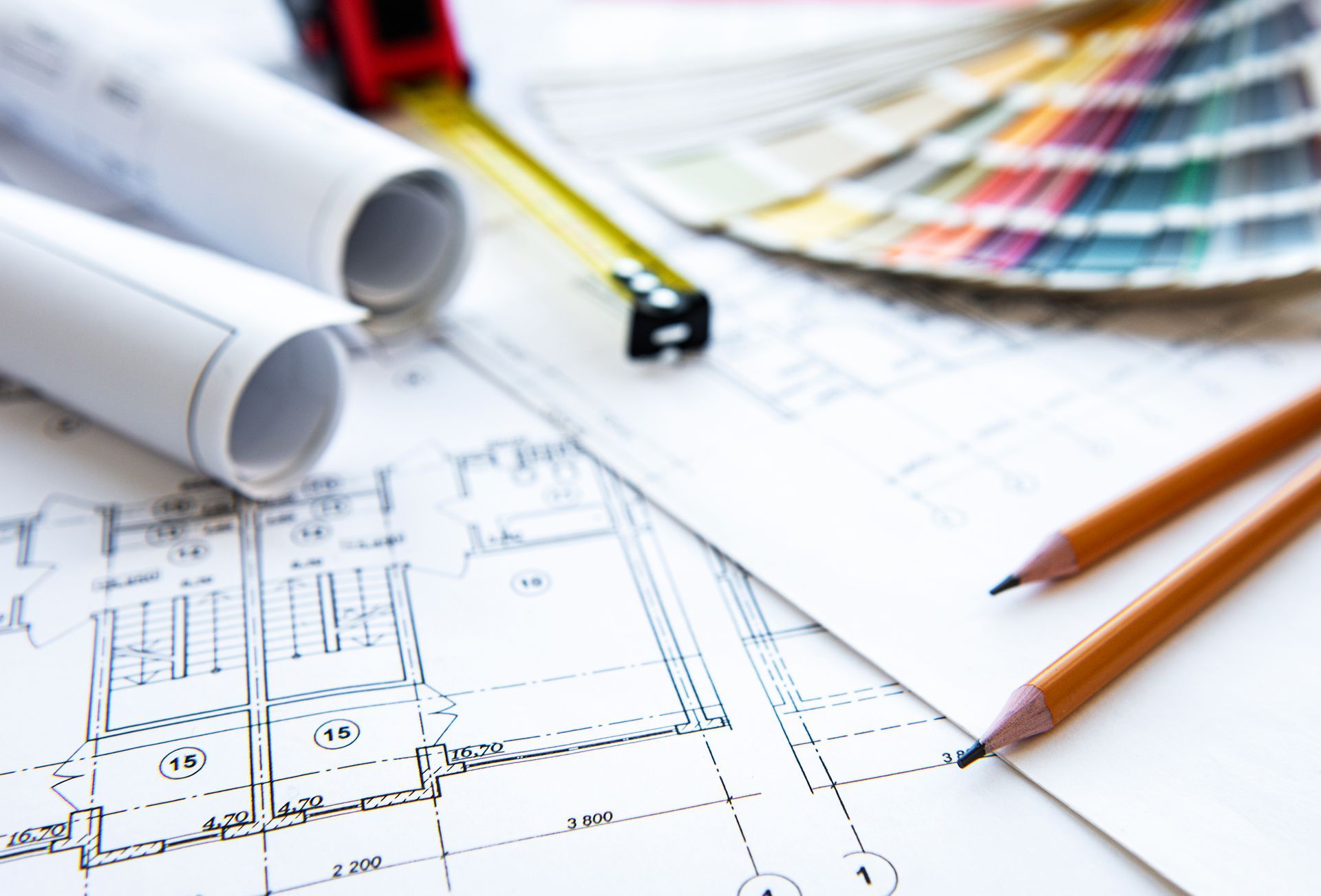 A pair of pencils sitting on top of a blueprint next to a tape measure.
