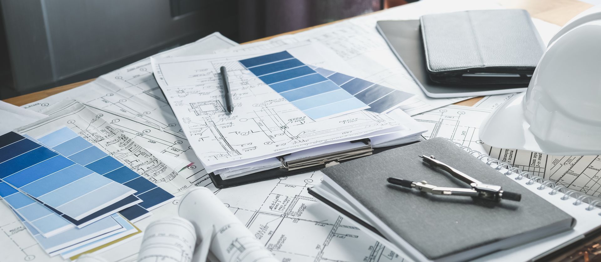 A desk with a hard hat , notebooks , a compass and a pen on it.
