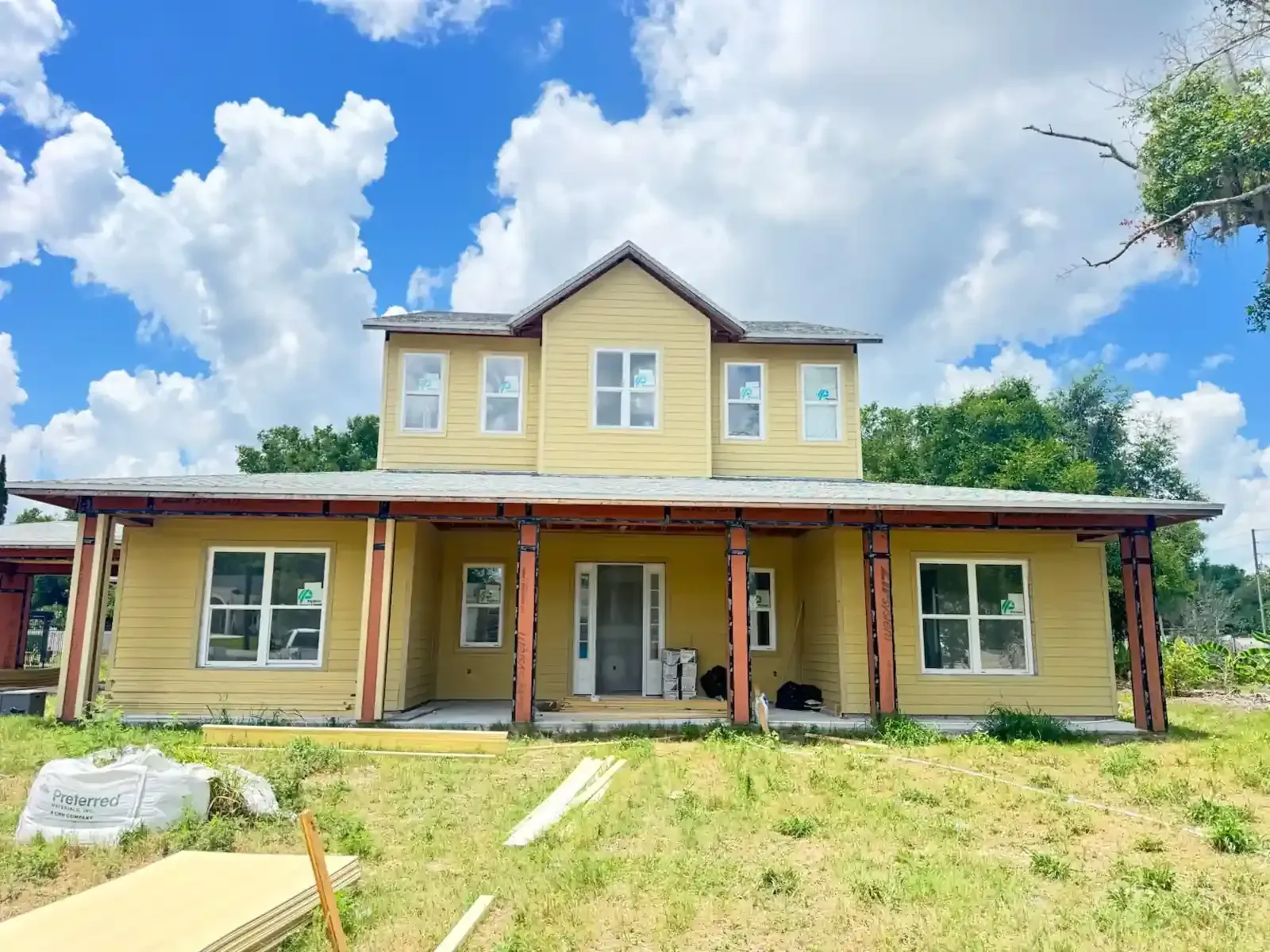 Yellow two-story house with a front porch and grassy yard under a blue sky