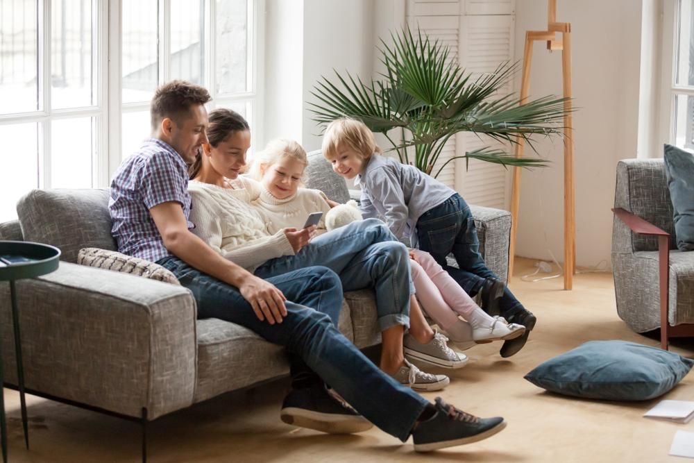 A Family Is Sitting On A Couch In A Living Room Looking At A Cell Phone — Howells & Co Legal & Conveyancing In Cessnock, NSW