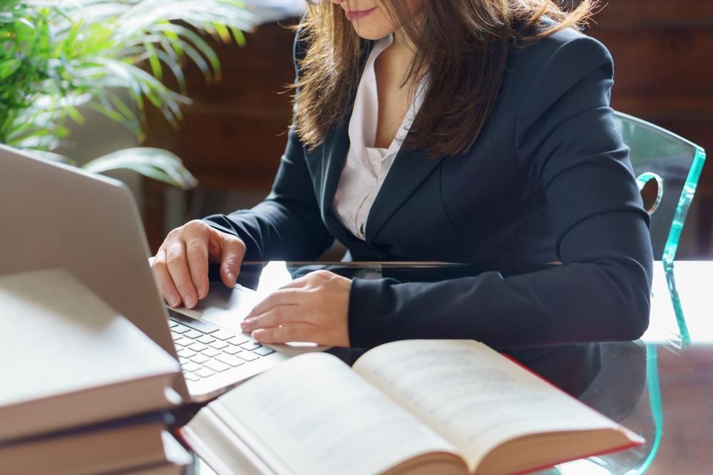A Woman Is Sitting At A Desk With A Book And A Laptop — Howells & Co Legal & Conveyancing In Albury, NSW