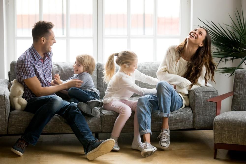 A Family Is Sitting On A Couch In A Living Room — Howells & Co Legal & Conveyancing In Wollongong, NSW