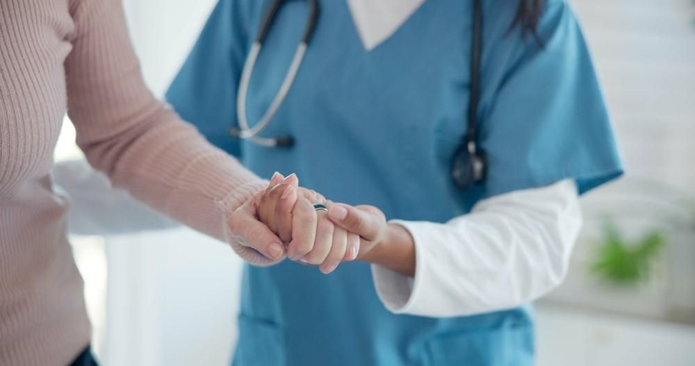 A Nurse Is Holding The Hand Of A Patient In A Hospital — Howells & Co Legal & Conveyancing In Cessnock, NSW