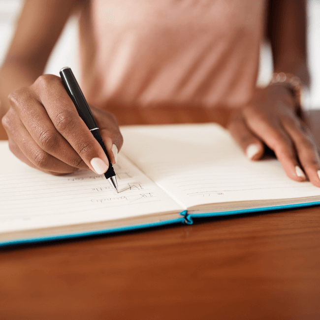A Woman Is Writing In A Notebook With A Pen — Howells & Co Legal & Conveyancing In Lake Cessnock, NSW